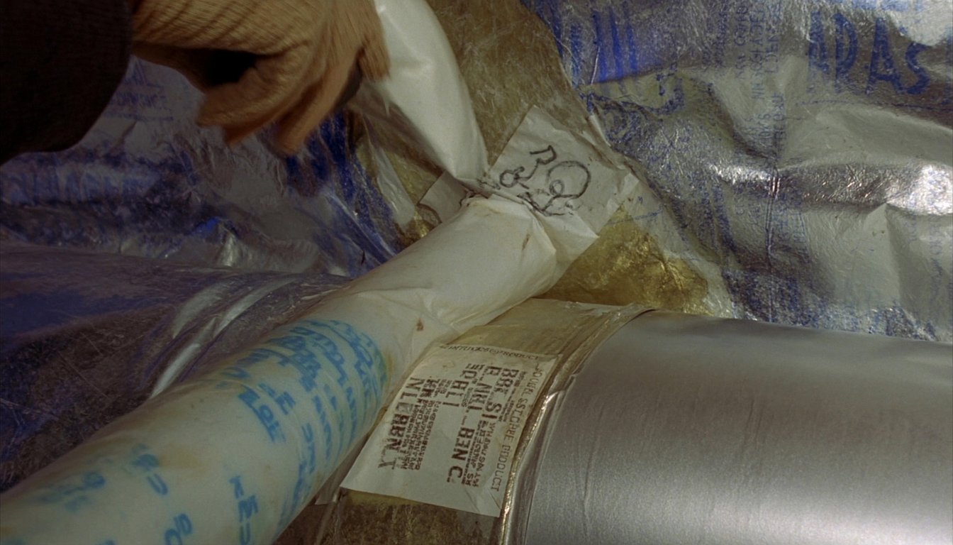Insulated flexible HVAC ductwork in a San Bernardino, California residential attic with a gloved technician hand applying mastic at a connection and R-8 silver insulation visible